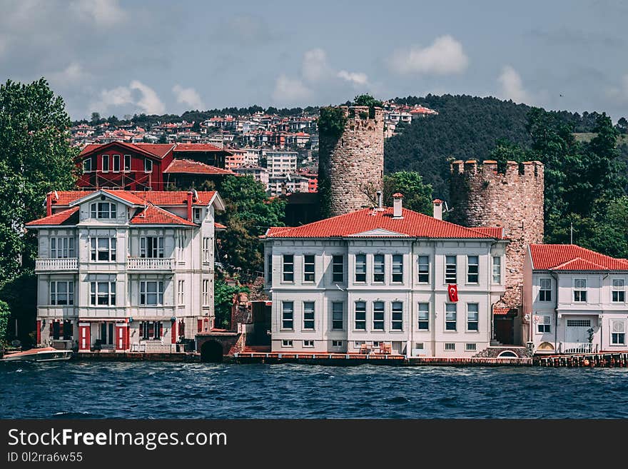 White and Red Concrete Structures Near Body of Water and Two Concrete Medieval Towers