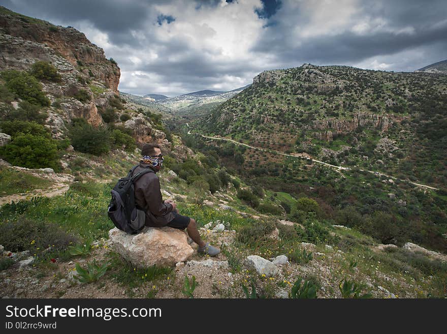 Man Sitting on Brown Boulder Top on Hill