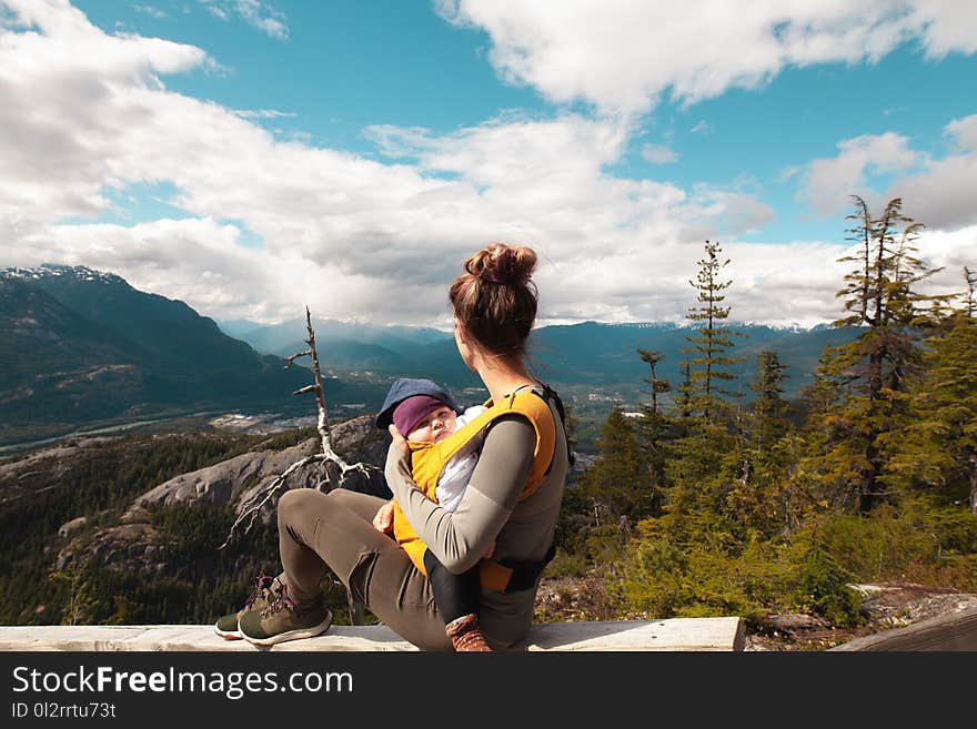 Woman Carrying Baby Sitting on Gray Surface