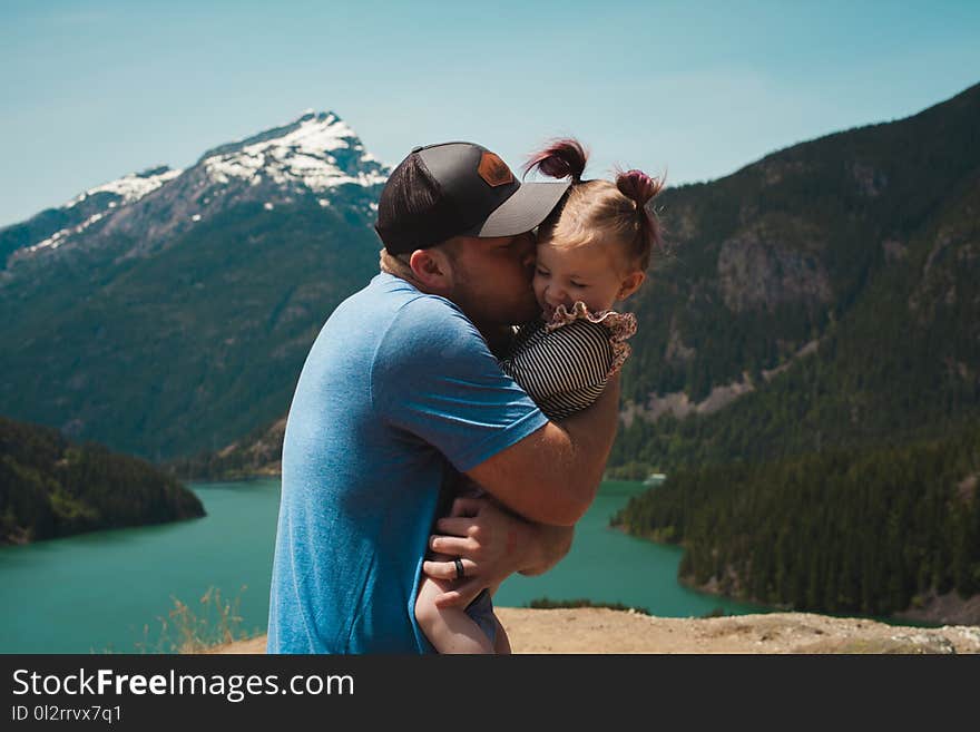 Man Wearing Blue Crew-neck T-shirt Holding Girl Near Mountains