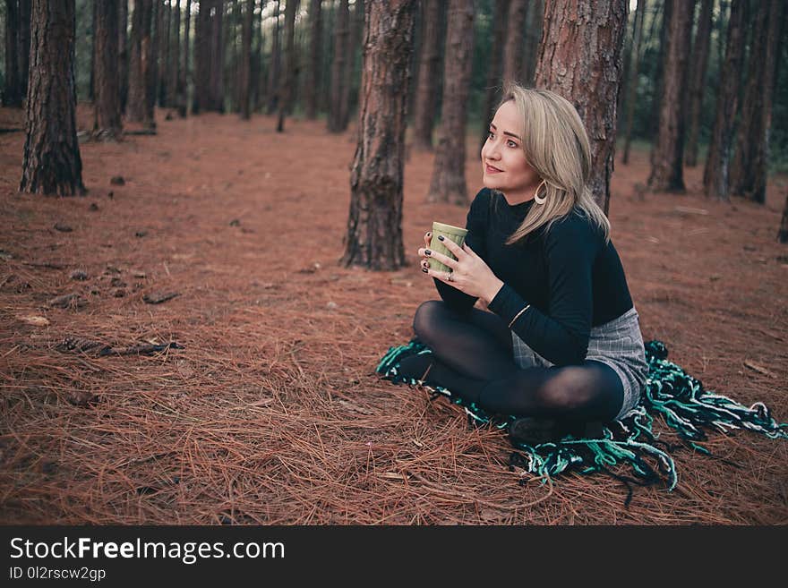 Woman in Black Sweater Sitting on Brown Ground While Holding Cup