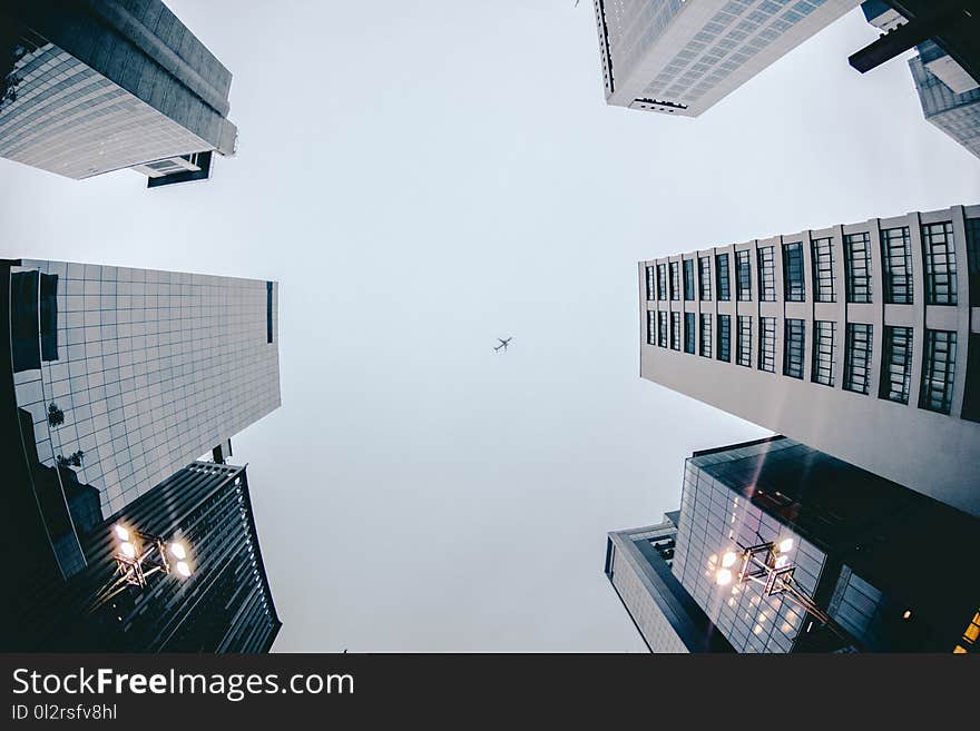 Low Angle Photography of Airplane Flying Above High Rise Buildings