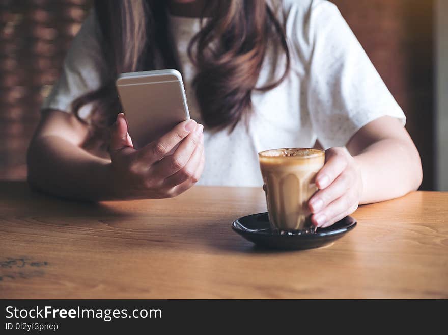 A woman holding , using and touching a smart phone while drinking coffee