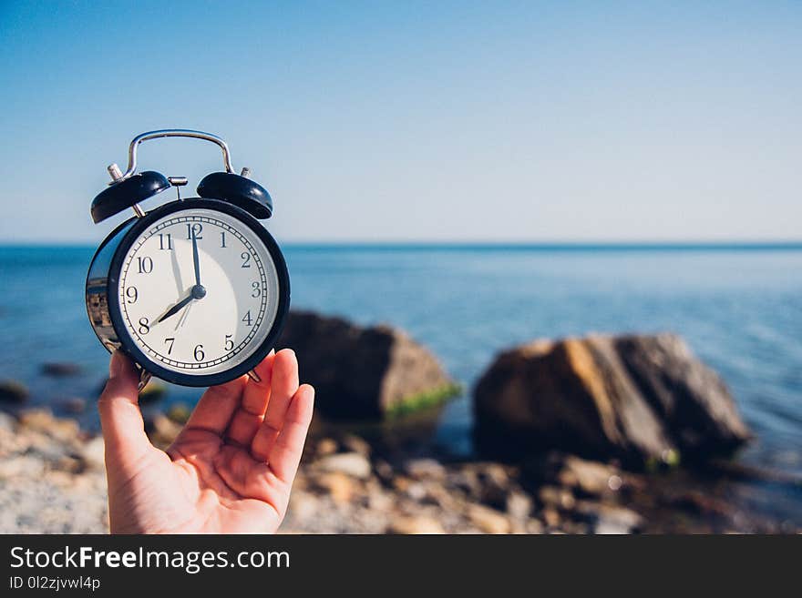 Hand hold watch on beach background.Alarm clock on sea and sand background different time with summer vacation.Vacation time conce