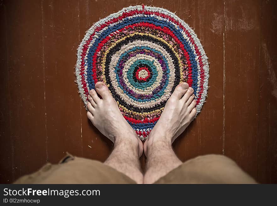 Legs men stand on a beautiful round homemade knitted colored rug. Close-up.