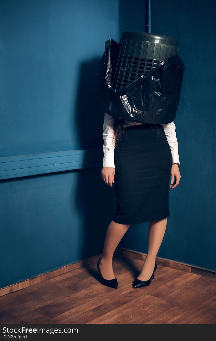 Crazy girl with garbage can on her head. Woman wearing white shirt blouse and formal black heels standing still in corner with trash can covering half of her body. Crazy girl with garbage can on her head. Woman wearing white shirt blouse and formal black heels standing still in corner with trash can covering half of her body.