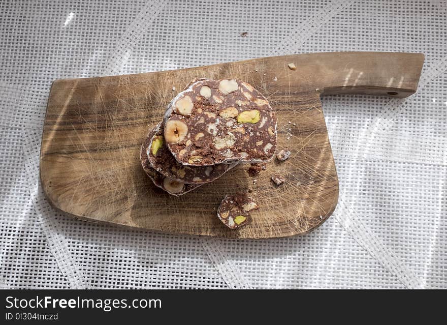 Slices of chocolate cake with hazelnuts and pistachios. Resting on a rustic wooden cutting board. View from above. Slices of chocolate cake with hazelnuts and pistachios. Resting on a rustic wooden cutting board. View from above.