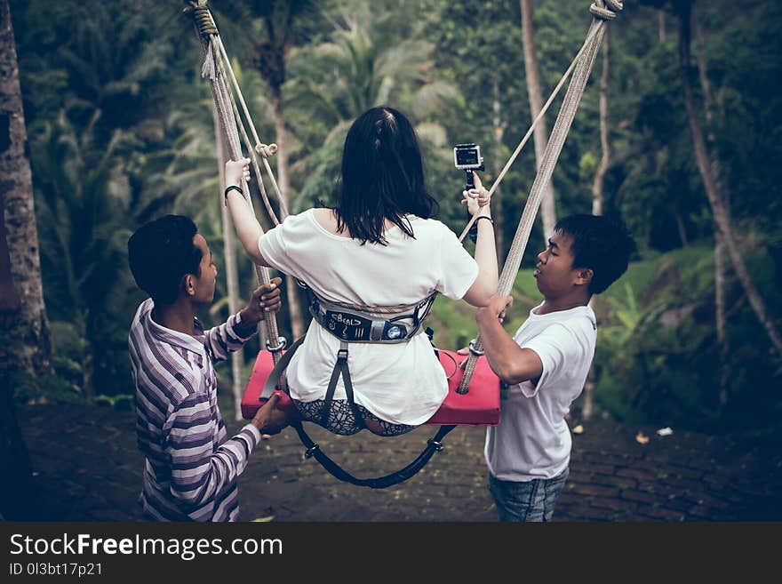 Two Men Assisting Woman Riding on Swing