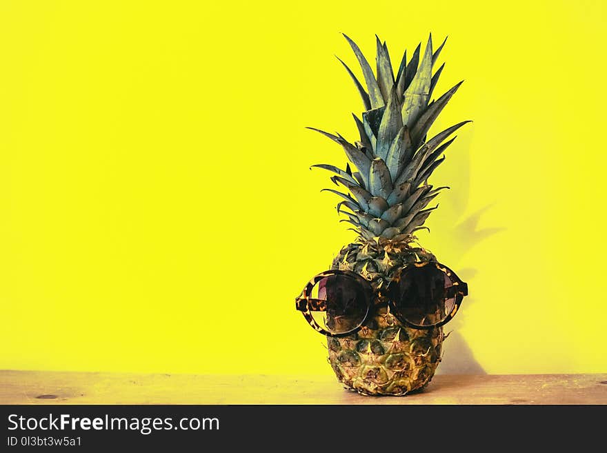 Green Pineapple Fruit With Brown Framed Sunglasses Beside Yellow Surface