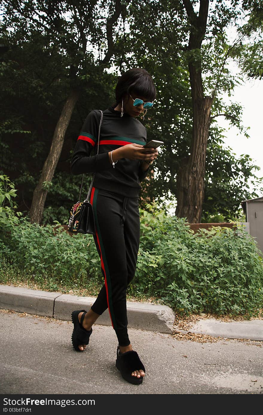 Woman in Black, Green, and Red Gucci Sweatshirt and Sweatpants Using Smartphone