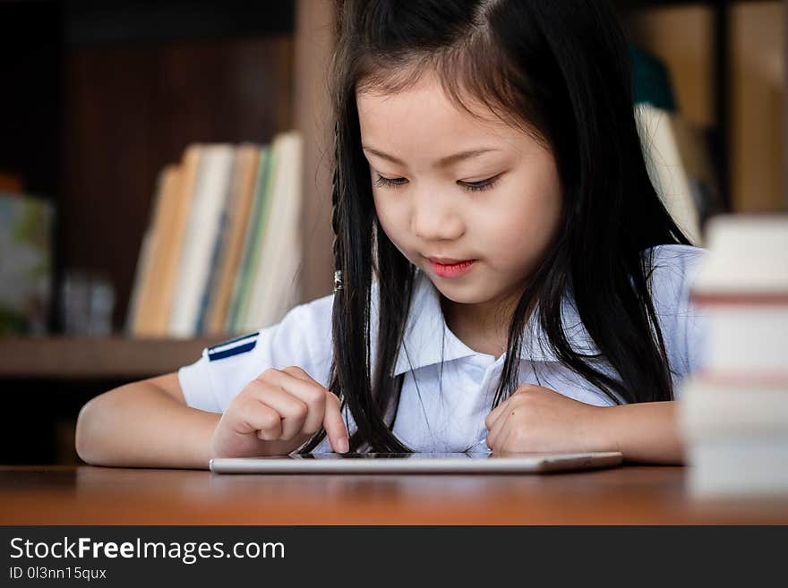 Cute girl smile sitdown and playing laptop computer in the library, children concept, education concept