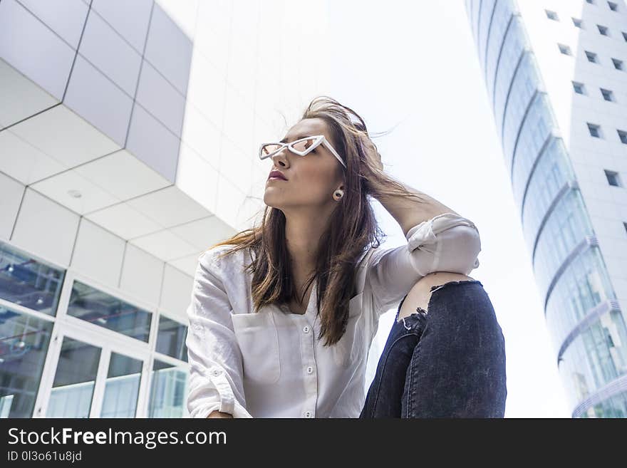 Low Angle Photography of Woman in White Shirt Sitting Beside Buildings