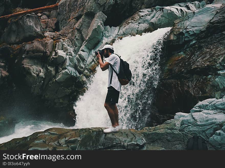 Man Wearing White T-shirt Holding Dslr Camera Near Waterfall