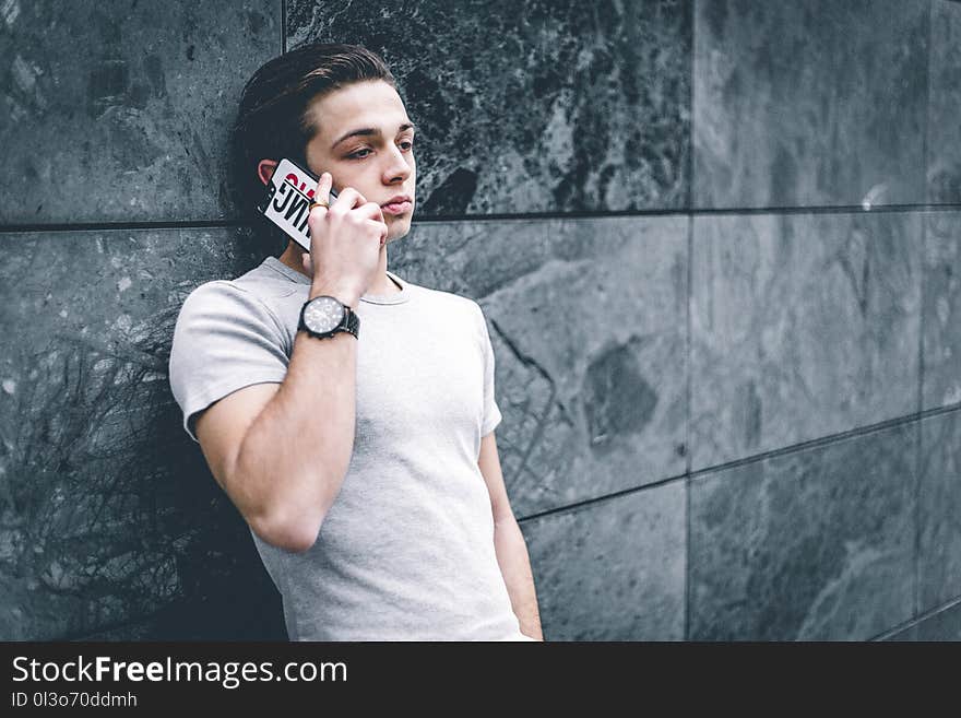 Man Wearing Gray Crew-neck T-shirt Leaning on Gray Wall