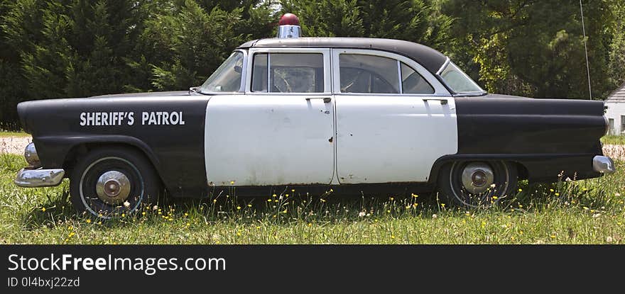 Side view of vintage antique Sheriff`s black and white patrol car in field. Side view of vintage antique Sheriff`s black and white patrol car in field.