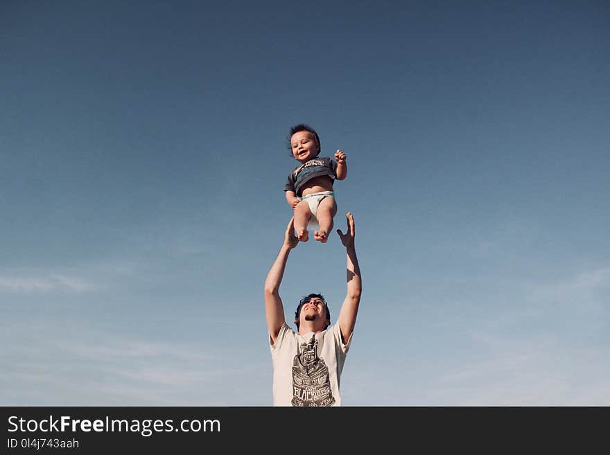 Photo of Man in Raising Baby Under Blue Sky