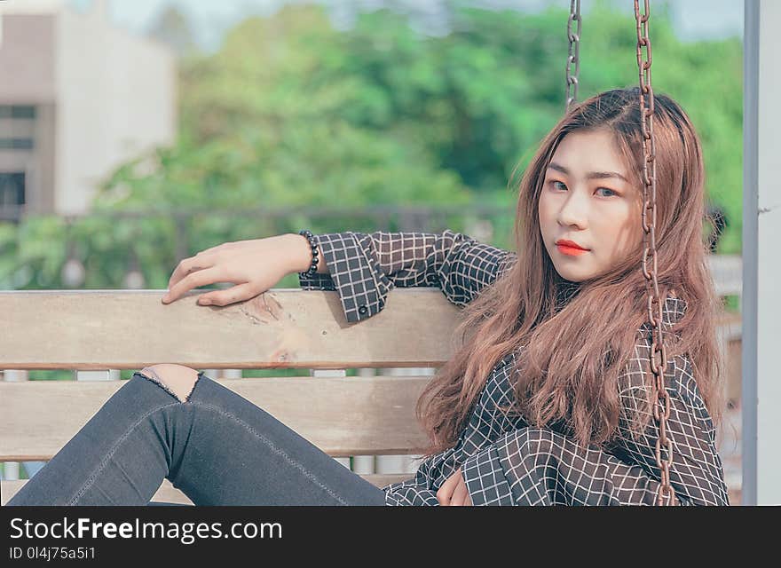 Woman in Black Button-up Long-sleeved Shirt Sitting on Brown Swing Bench