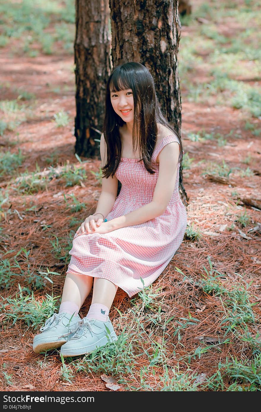 Girl&#x27;s Pink Sleeveless Dress Sits Beside Black Tree Trunk at Daytime