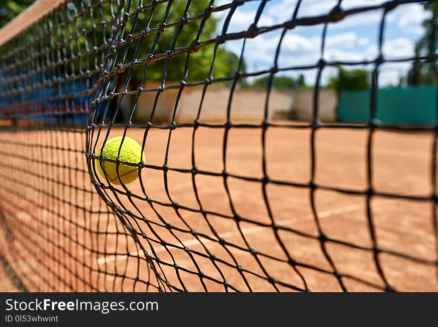 Tennis ball hitting into the net on the court outdoors. Sun is shining. Closeup. Horizontal. Tennis ball hitting into the net on the court outdoors. Sun is shining. Closeup. Horizontal.