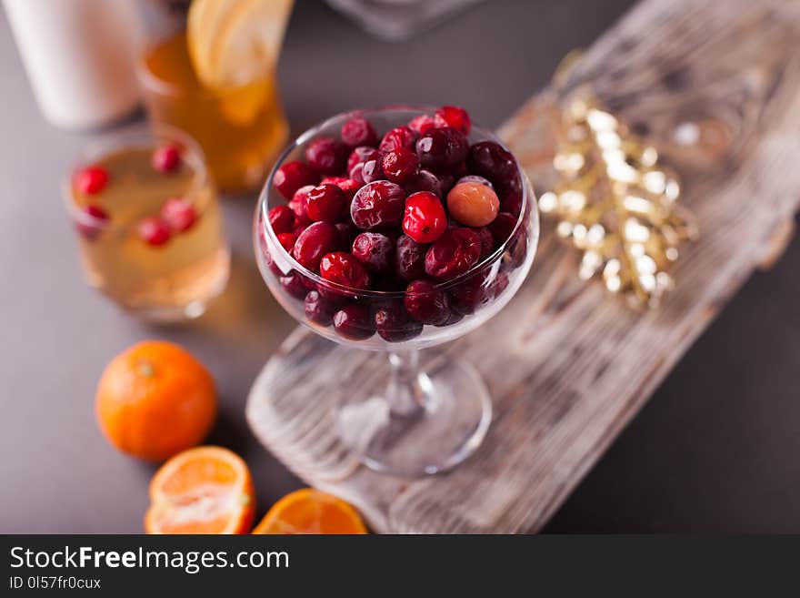 Cranberry in glass bowl on a wooden tray, tangerines, a glass with cider, selective focus.