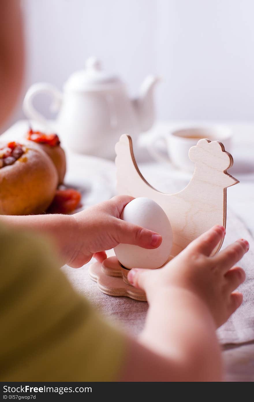 Easter breakfast or lunch - egg in a wooden stand, tea and baked apples on a light background, Provence. children`s hands reach for the egg