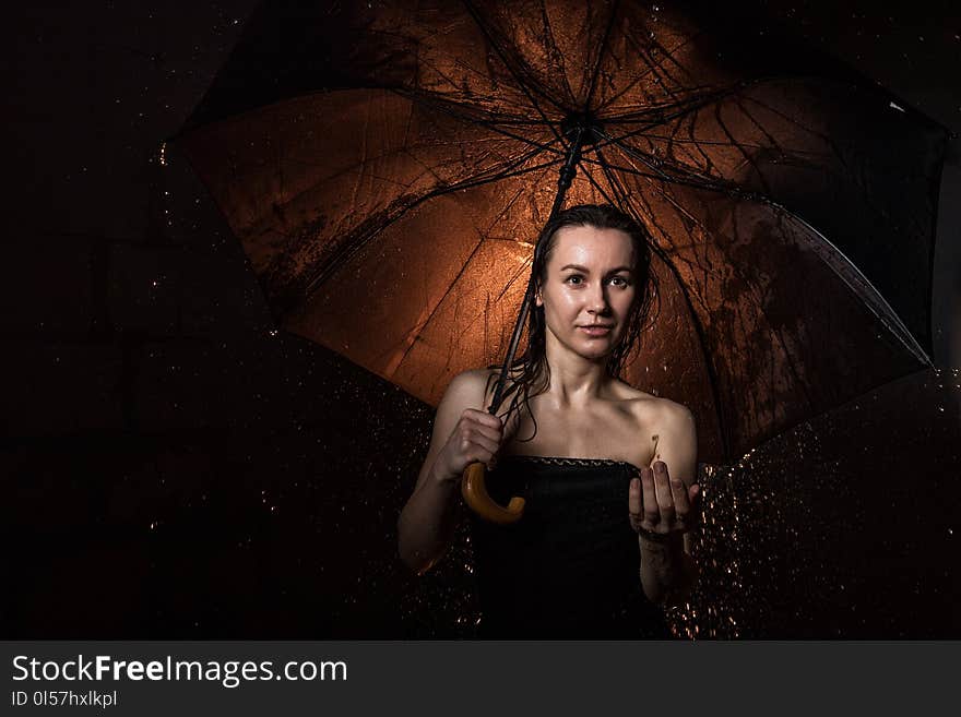 Girl in black dress with umbrella and drops of water during a photoshoot