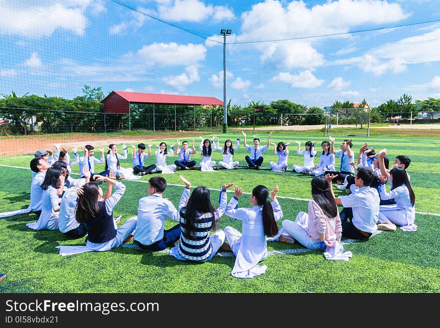 People Sitting on Green Lawn Grass While Doing Hands Up at Daytime