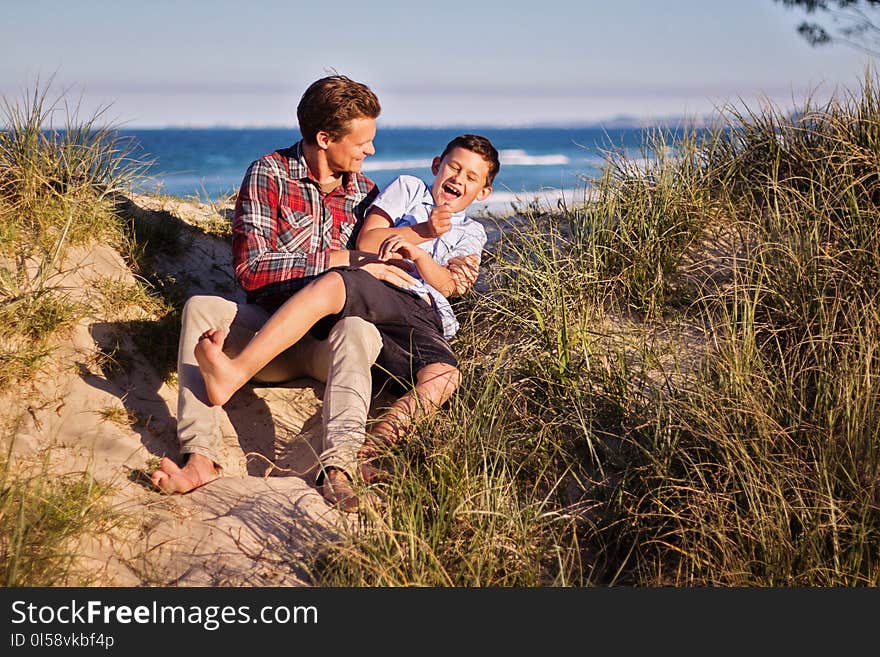 Man and Boy Sitting on Floor Near Body of Water