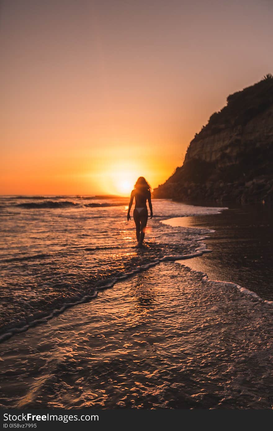 Woman in Bikini on Body of Water Behind Mountain during Golden Hour