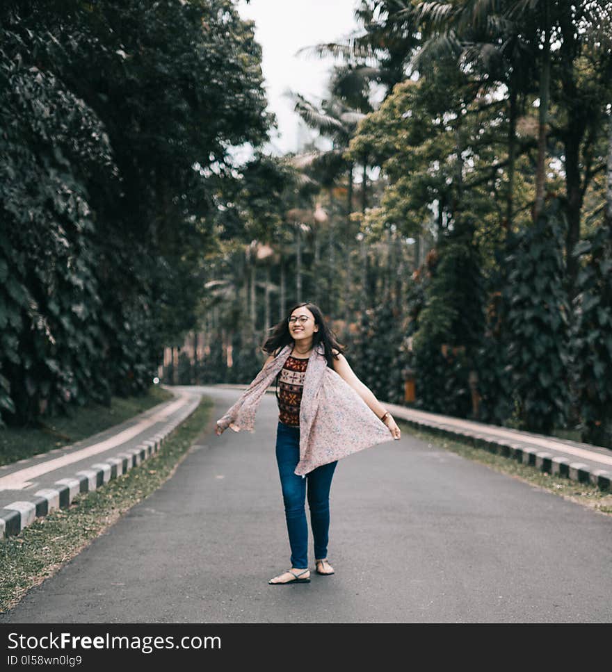 Woman Standing on Road Between Trees