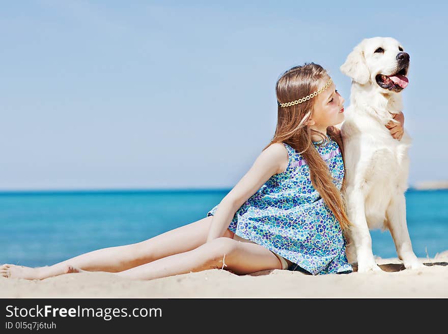 Young girl with her dog by seaside playing on the sand