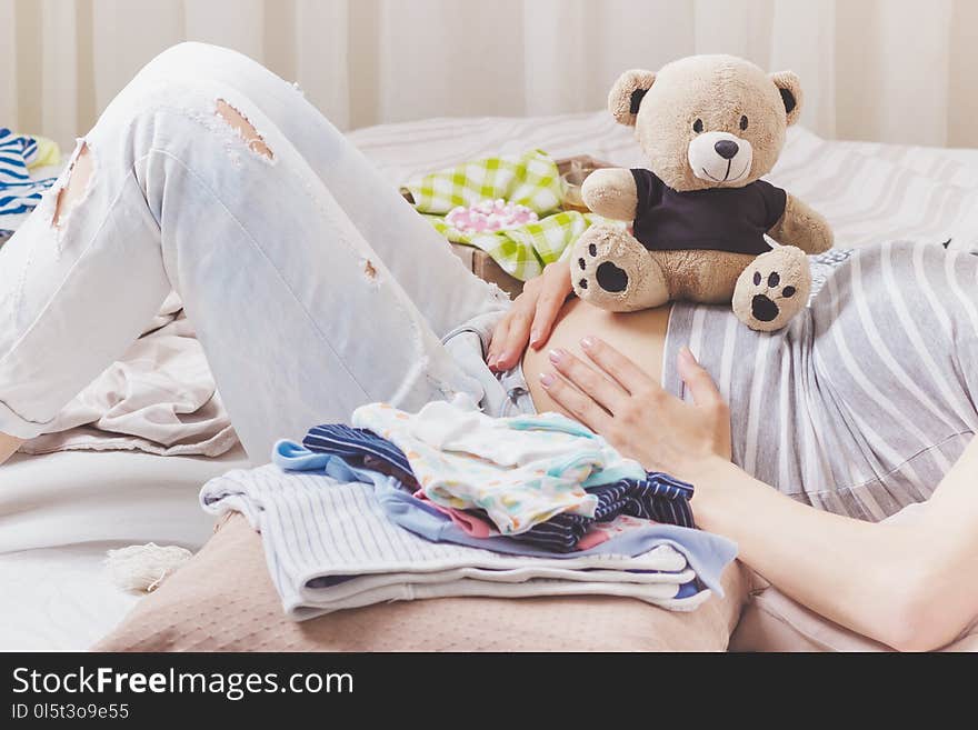 Pregnant woman with a teddy bear and various clothes for a newborn, top view