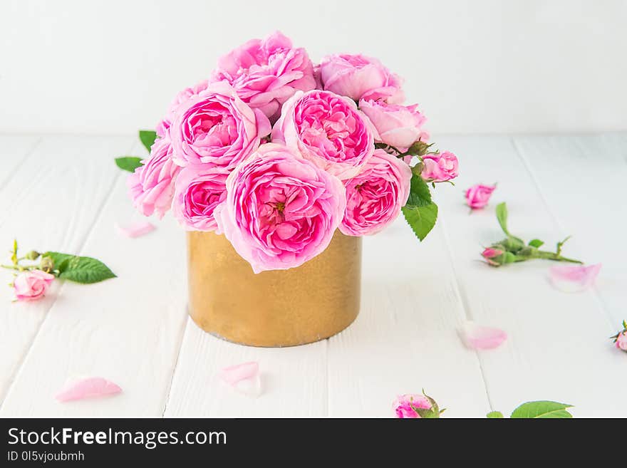 Close up tender pink tea roses bouquet in vintage golden pot on the white wooden table. Floral background. Postcard mock up. Summer, spring flowers. Selective focus. Copy space