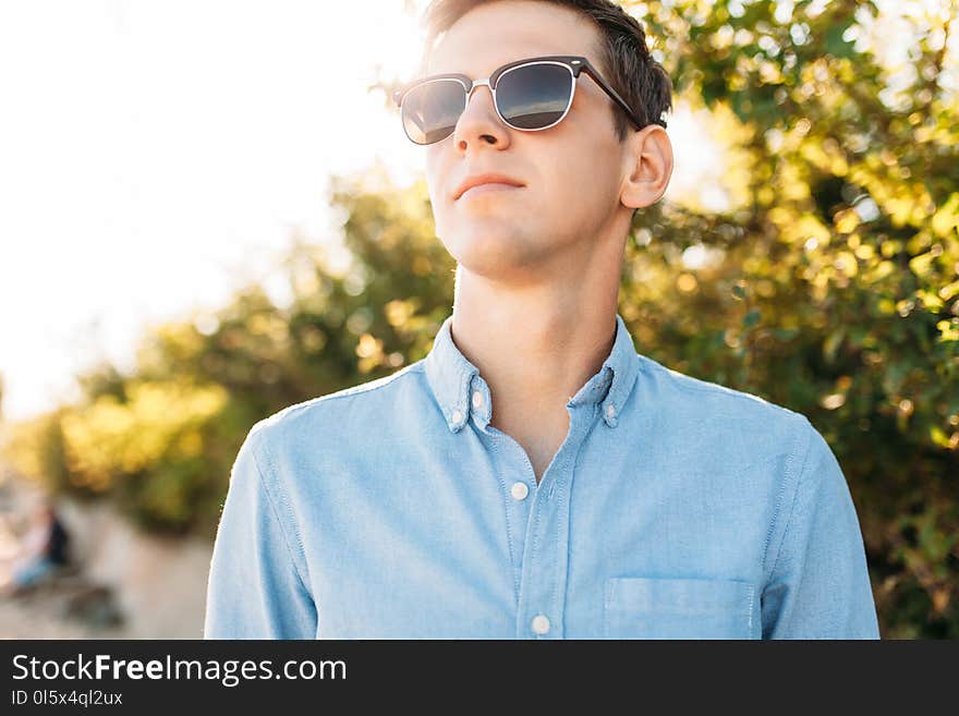 Beautiful stylish guy with glasses, posing on the beach, at sunset, hipster posing in stylish clothes, for advertising, text inser