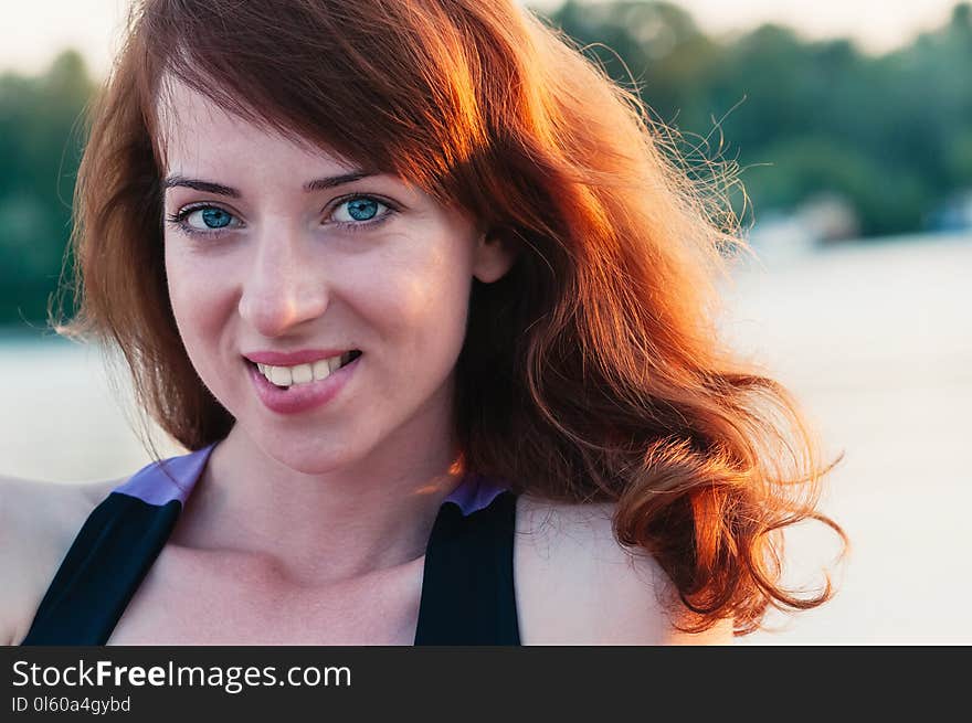 Close up portrait of a young beautiful ginger haired woman, biting her lip in a smile, white teeth, looking at camera, on water summer nature background. Close up portrait of a young beautiful ginger haired woman, biting her lip in a smile, white teeth, looking at camera, on water summer nature background