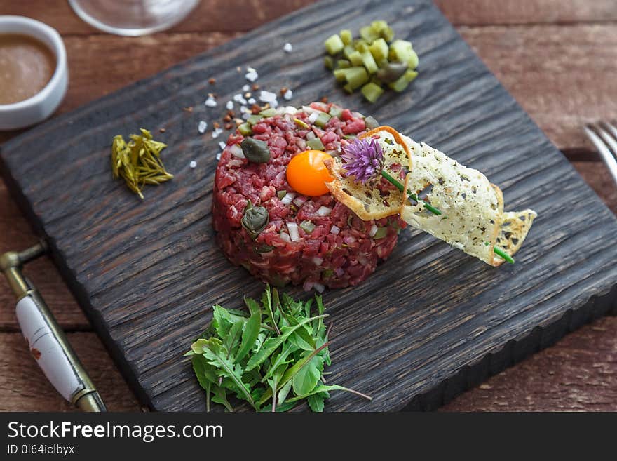 Beef tartare with capers, pickled cucumber and fresh onions on dark background.