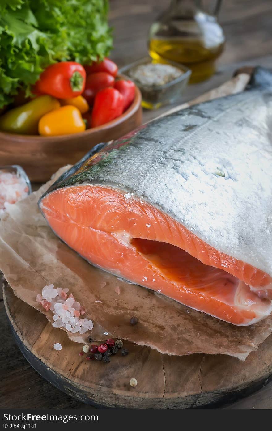 A large piece of salmon lies on a wooden table for cooking. Horizontal frame.