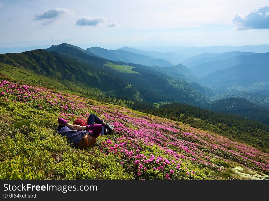 The landscape with the high mountains. Sky with clouds. Forest road. On the lawn of the rhododendrons the girl is laying. Eco tourism. Charming summer day.