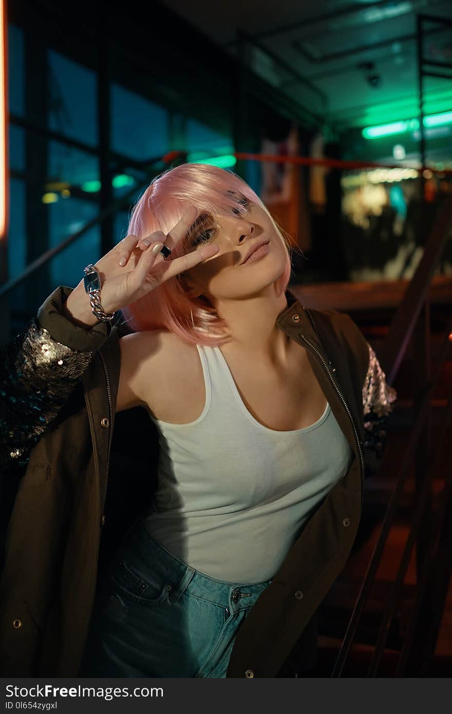 Hot girl with pink hair white casual t-shirt and stylish jacket posing while resting in a modern night club, industrial style cafe, with neon lamps glow, windows in background. Hot girl with pink hair white casual t-shirt and stylish jacket posing while resting in a modern night club, industrial style cafe, with neon lamps glow, windows in background.