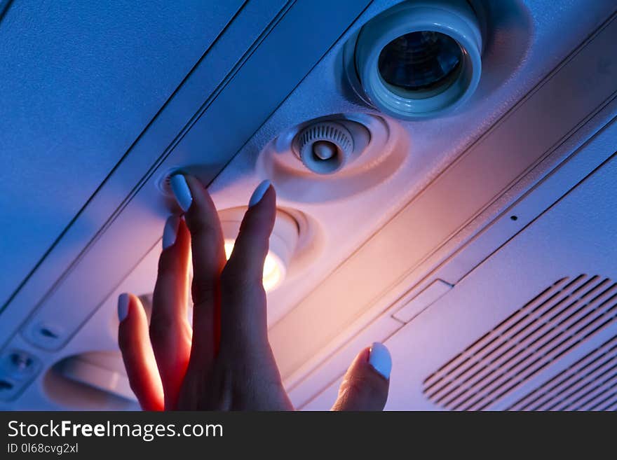 The passanger hand closeup turn on the light in the airplane cabin. Dark blue background with yellow light.