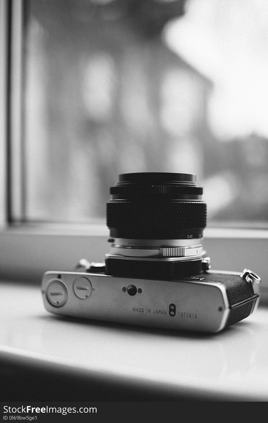 Grayscale Photography of Camera Near Window