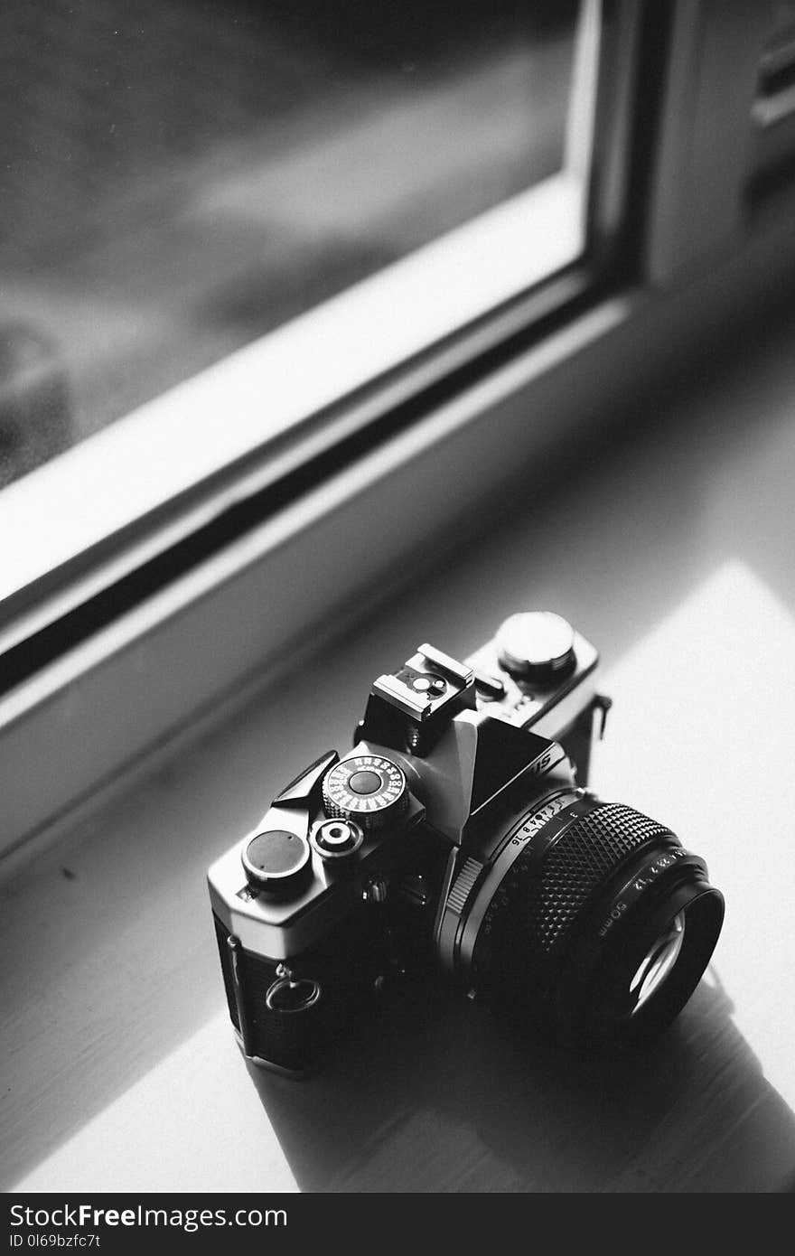 Grayscale Photo of Classical Camera Near Window