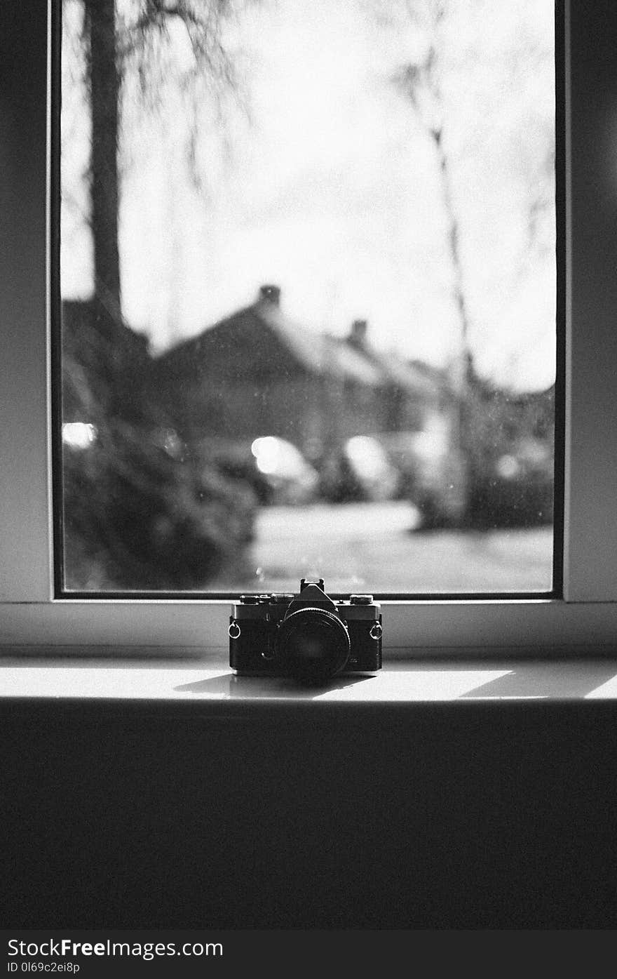 Grayscale Photo of Camera Beside Window