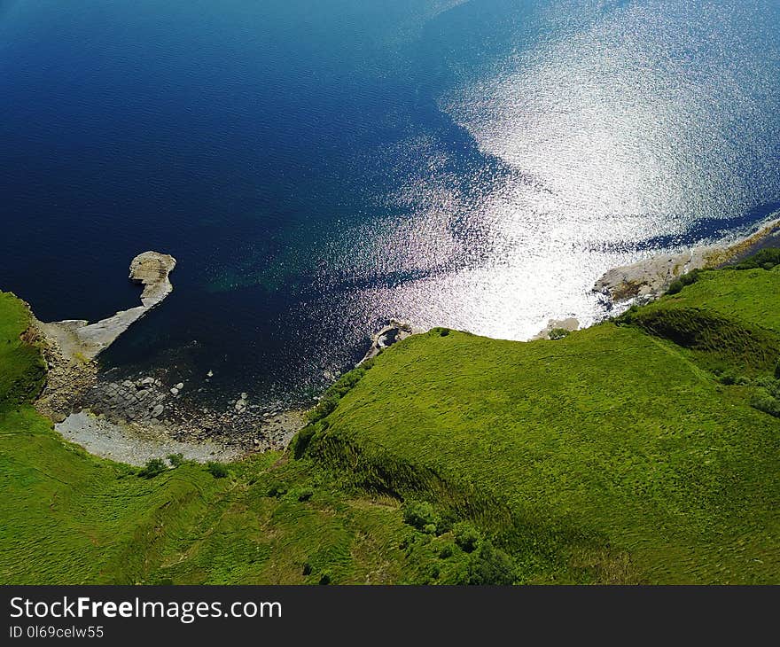 Green Grass Land With Blue Body of Water Below