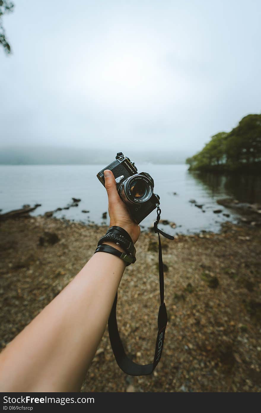 Person Holding Black Camera Front Body of Water