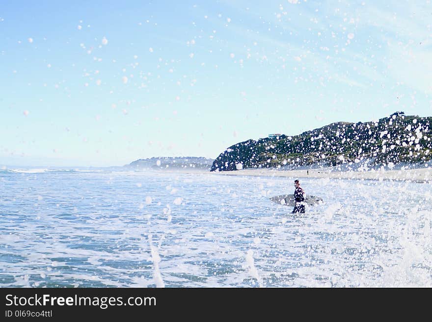 Person Carrying Surfboard Walking on Sea Water