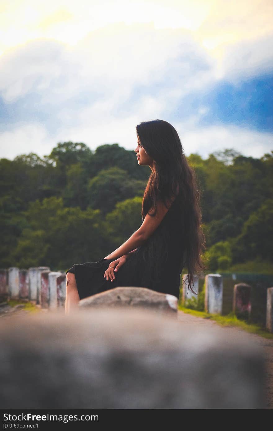 Woman Sitting on Concrete Pillar