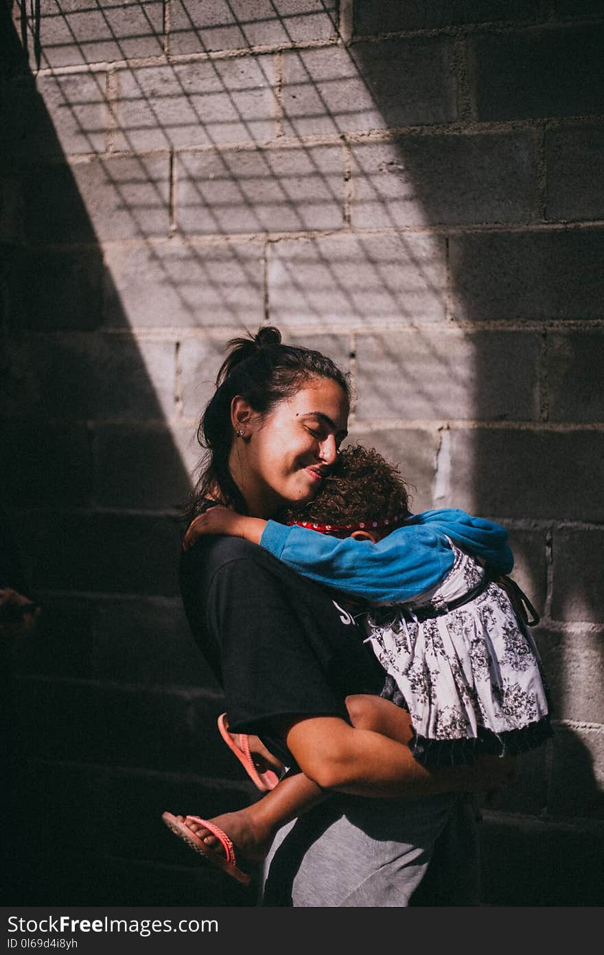 Woman Holding Girl Beside Gray Wall