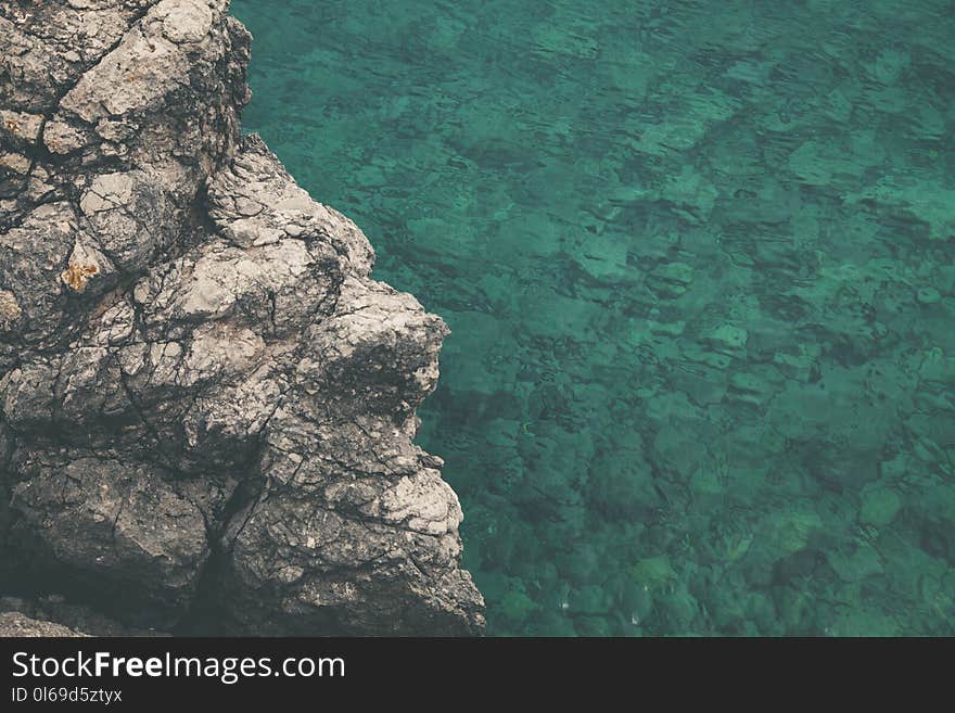 Brown and Gray Rock Formation Beside Calm Body of Water at Daytime