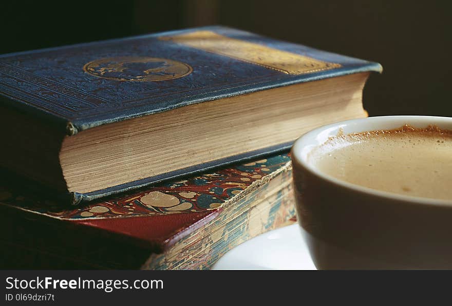 Book Beside Cup Filled With Brown Liquid